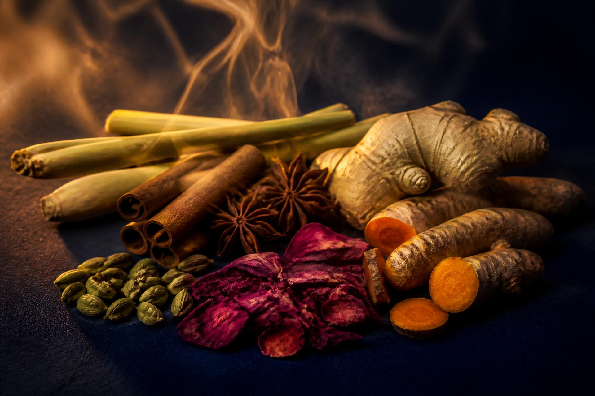 Whole spices, herbs and rhizomes arranged on a deep blue surface with drifting steam